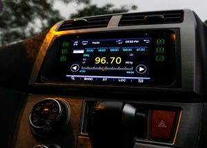 The close up view of the smart multimedia touchscreen radio panel in the car. The close up view of the smart multimedia touchscreen radio panel in the car with street light flare during the rain. Car system control using panel button screen interface modern design.